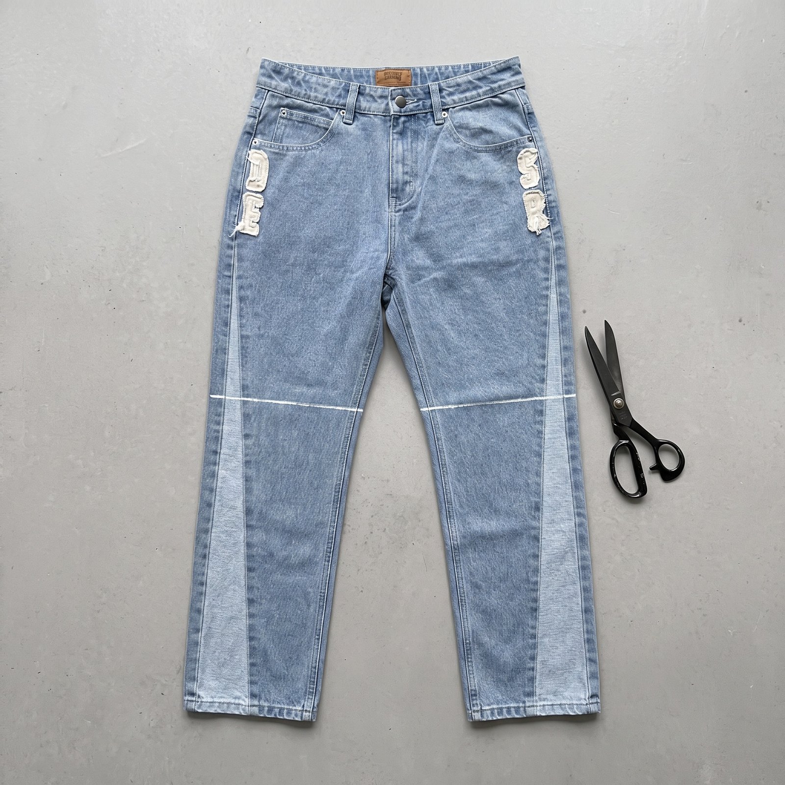 Lange Jeans mit Kreidelinie über dem Knie, daneben eine Schere